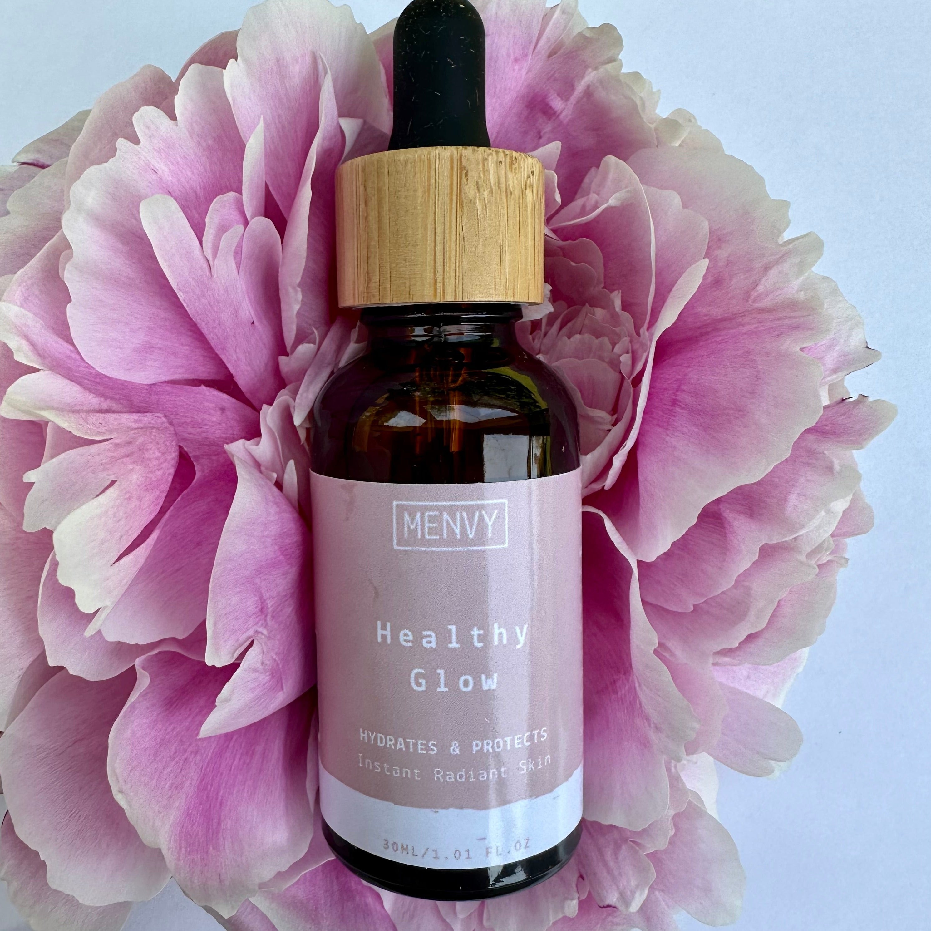 Healthy Glow face serum for menopause skin. Bottle is resting on a pink peony.