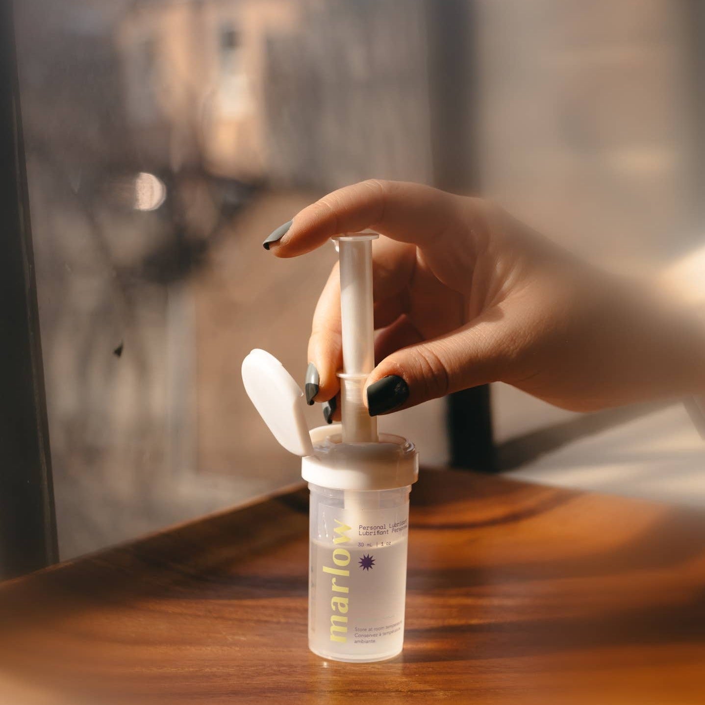 A photo of a woman's hand putting a tampon applicator into a jar of Marlow lubricant