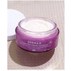 A purple glass jar of Derma E Crepey Skin Repair Treatment is open with the cap next to it, showing the white cream inside of the jar.